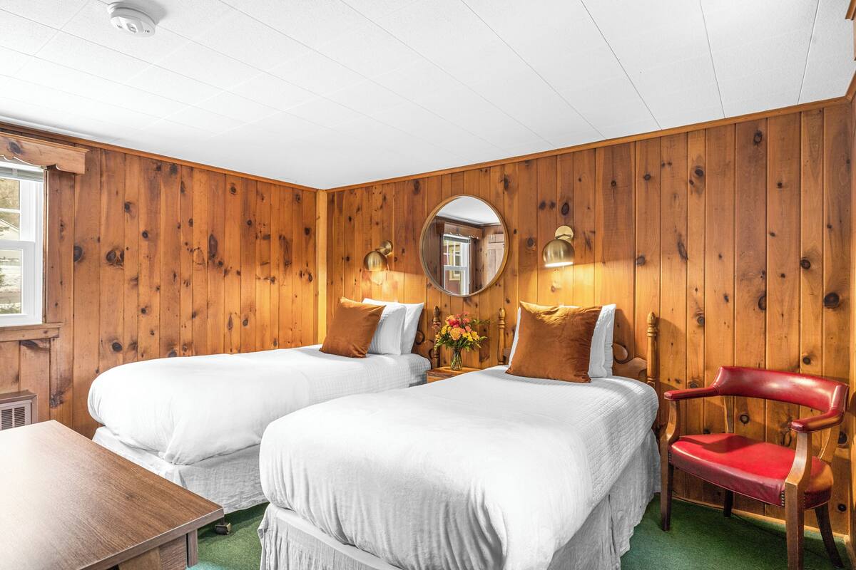 A room with two beds, a wooden wall, a mirror, and a red chair.