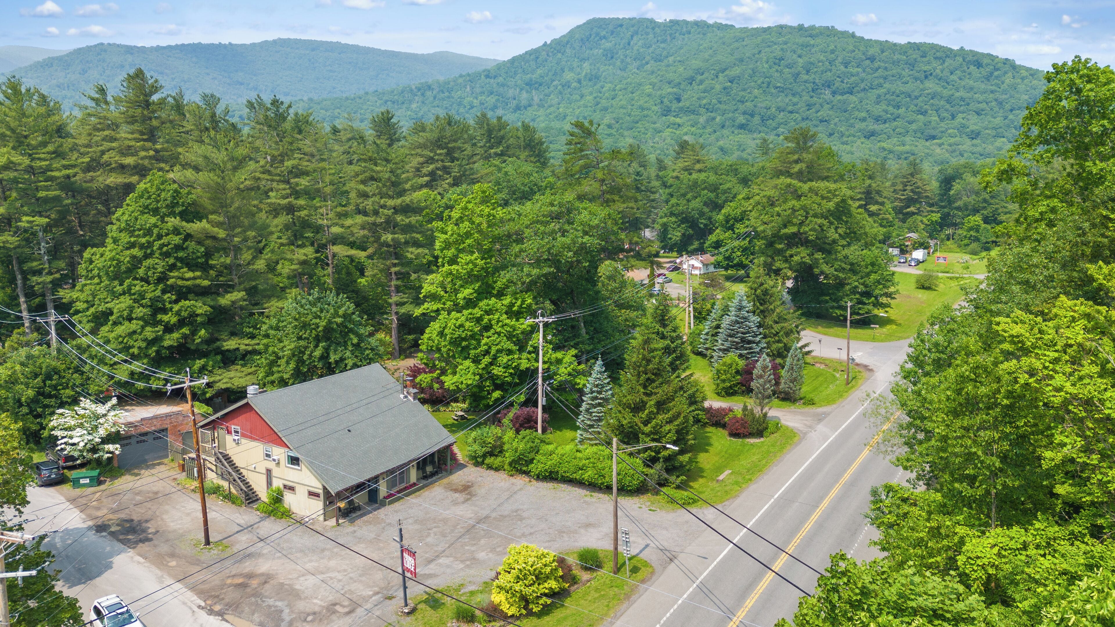 A rural area with a small building, possibly a post office or community center, surrounded by lush greenery and a mountain in the background.