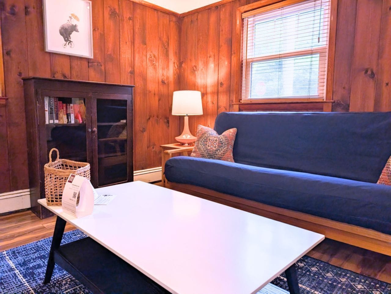 Una habitación acogedora con un sofá azul, una mesita de café blanca, una cesta de mimbre y una lámpara.