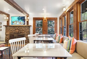 Un comedor con chimenea de piedra, vigas de madera y ventanas amplias.