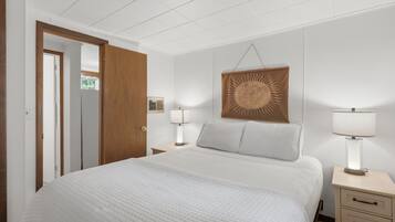 A hotel room with a bed, bedside lamps, a wooden door, and a wall-mounted sun decoration.