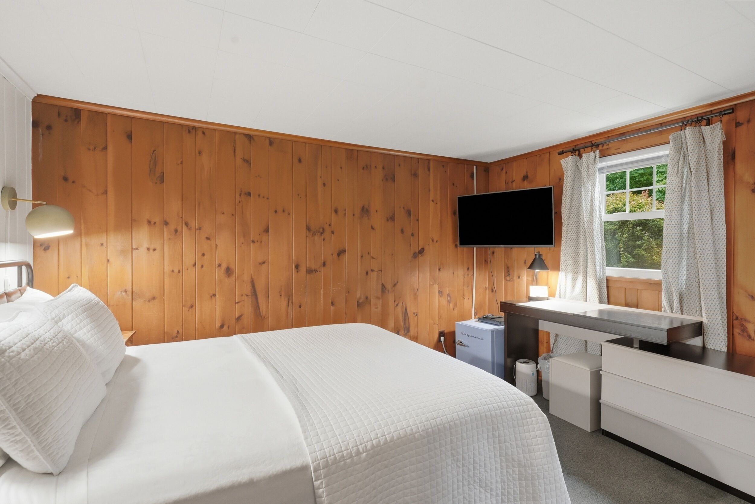 Ein Schlafzimmer mit einem Bett, einem Schreibtisch, einem Fernseher und einem Fenster mit Vorhängen.