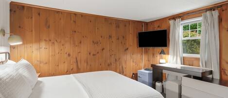 Ein Schlafzimmer mit einem Bett, einem Schreibtisch, einem Fernseher und einem Fenster mit Vorhängen.