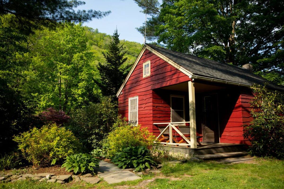 A red cabin with a porch, surrounded by lush greenery and trees.