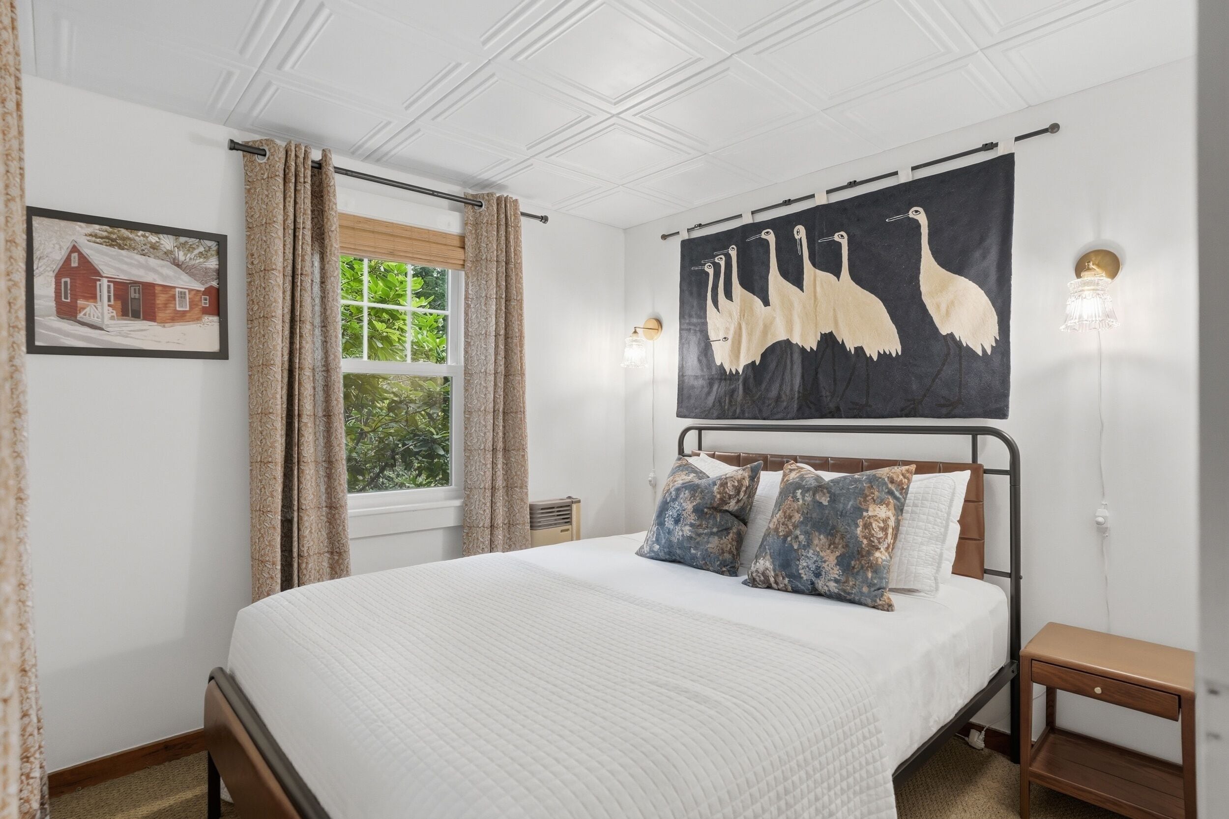 Un dormitorio con cama, un cuadro, una ventana con cortinas, una lámpara de pared y un adorno en la pared.