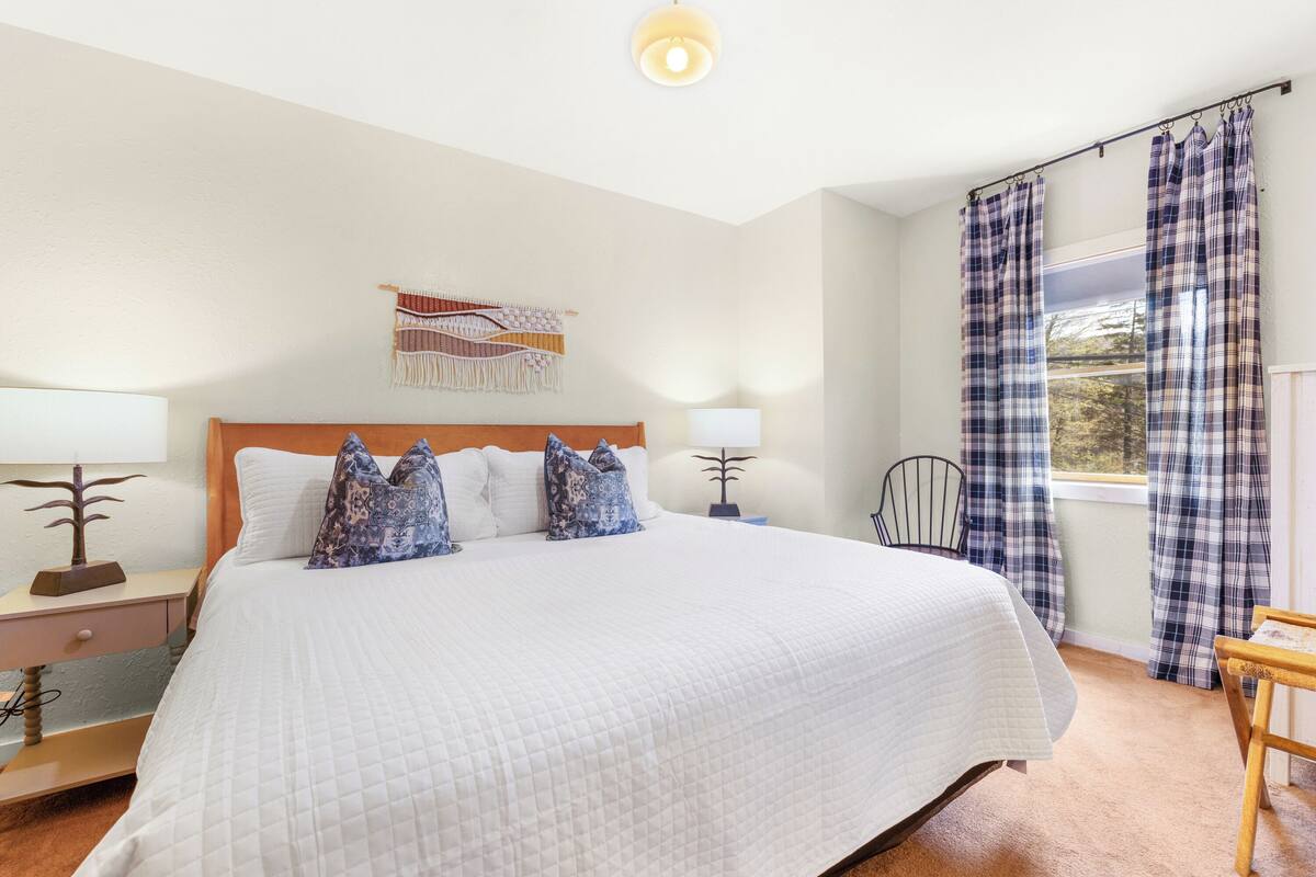 A neatly made bed with a white quilt, a wooden headboard, and a wall-mounted tapestry.