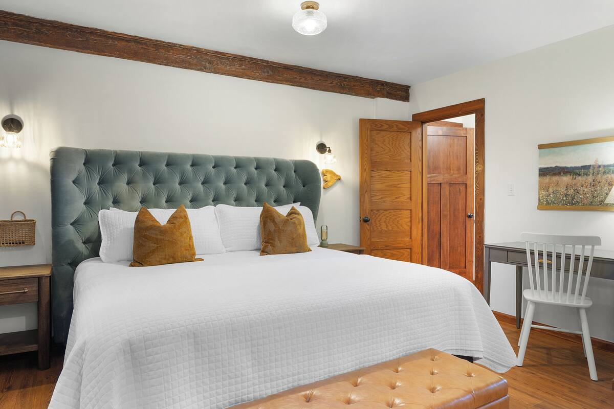 A bedroom with a large bed, a wooden headboard, a white desk, and a chair.