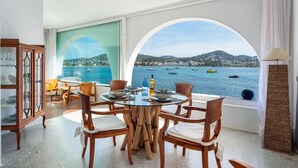 Un comedor con vista al mar, que incluye una mesa redonda, sillas de madera y un aparador de vidrio.