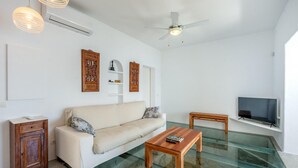 Una sala de estar moderna con un sofá blanco, una mesa de centro de madera, una mesa con cubierta de vidrio, un televisor y paneles decorativos de madera en la pared.