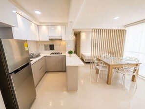 A modern kitchen with a built-in refrigerator, stove, and sink. There is a dining area with a wooden table and chairs. - Apartamentos Palmar - by SOHO (Puerto Colombia)