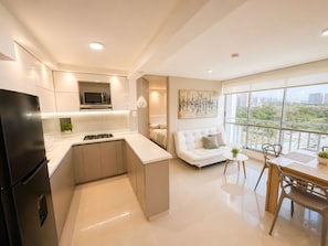 A modern kitchen with a built-in microwave, a gas stove, and a refrigerator. There is a dining area with a table and chairs, and a sofa in the living room.