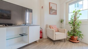 Een woonkamer met een flatscreen televisie, een bank, een kamerplant en een raam.