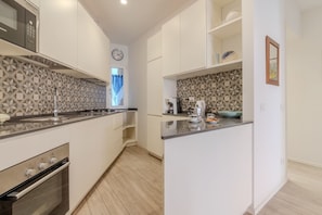 Une cuisine moderne avec des meubles blancs, un four encastré, un micro-ondes et un crédence décorée.