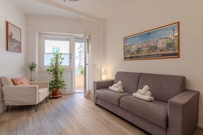Una sala de estar con un sofá, una silla, una planta en maceta y una puerta que da al exterior.