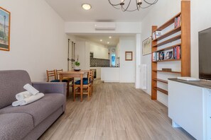 A modern living room with a sofa, dining table, chairs, a bookshelf, and a TV.