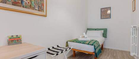 A bedroom with a bed, a desk, a chair, and a radiator.