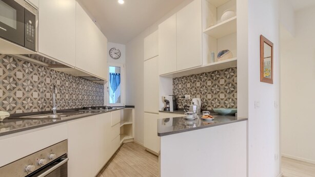 Een moderne keuken met witte kastjes, een inbouwoven, een magnetron en een decoratieve spatwand.