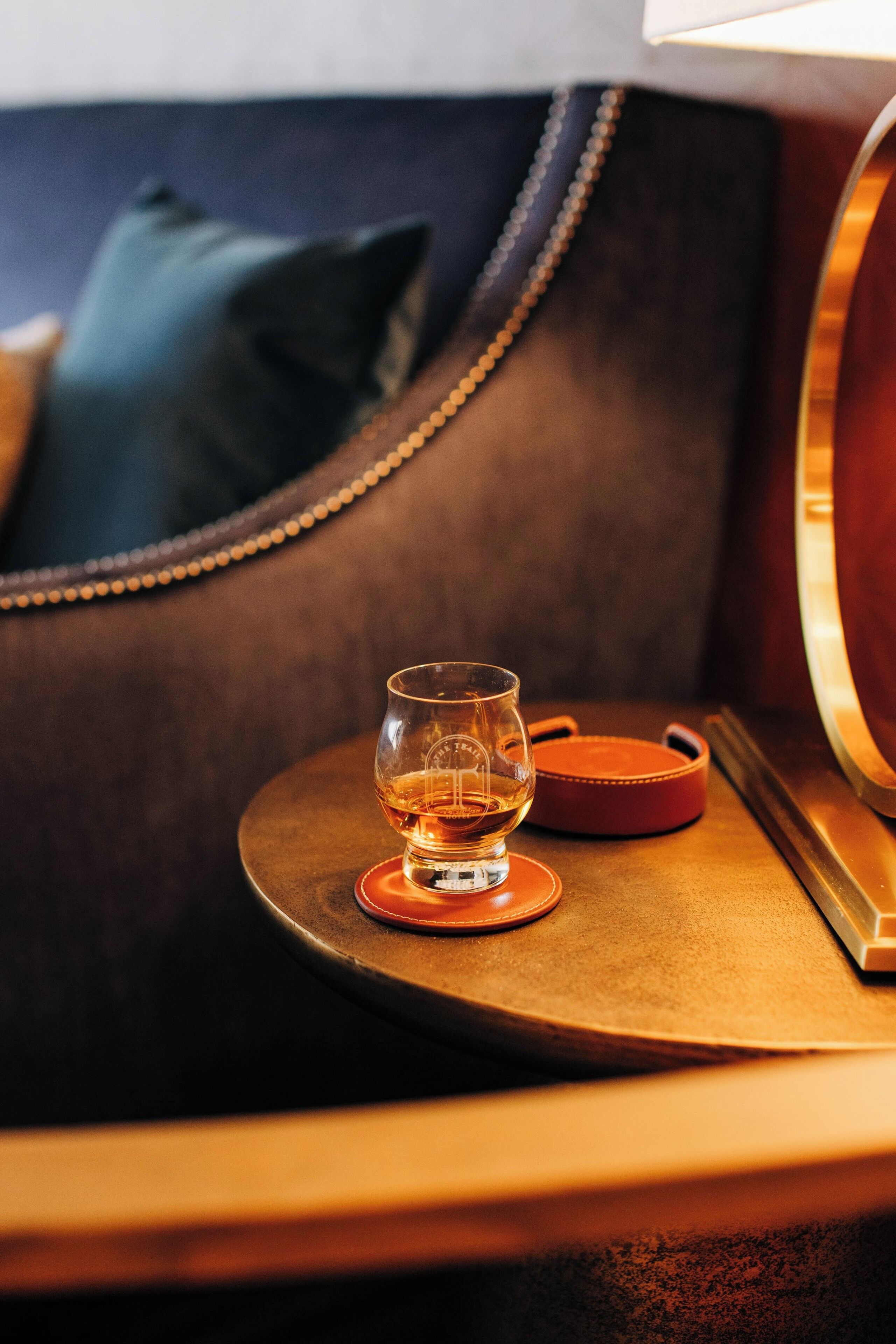 A cozy seating area with a leather couch, a glass of whiskey, and a small round table.