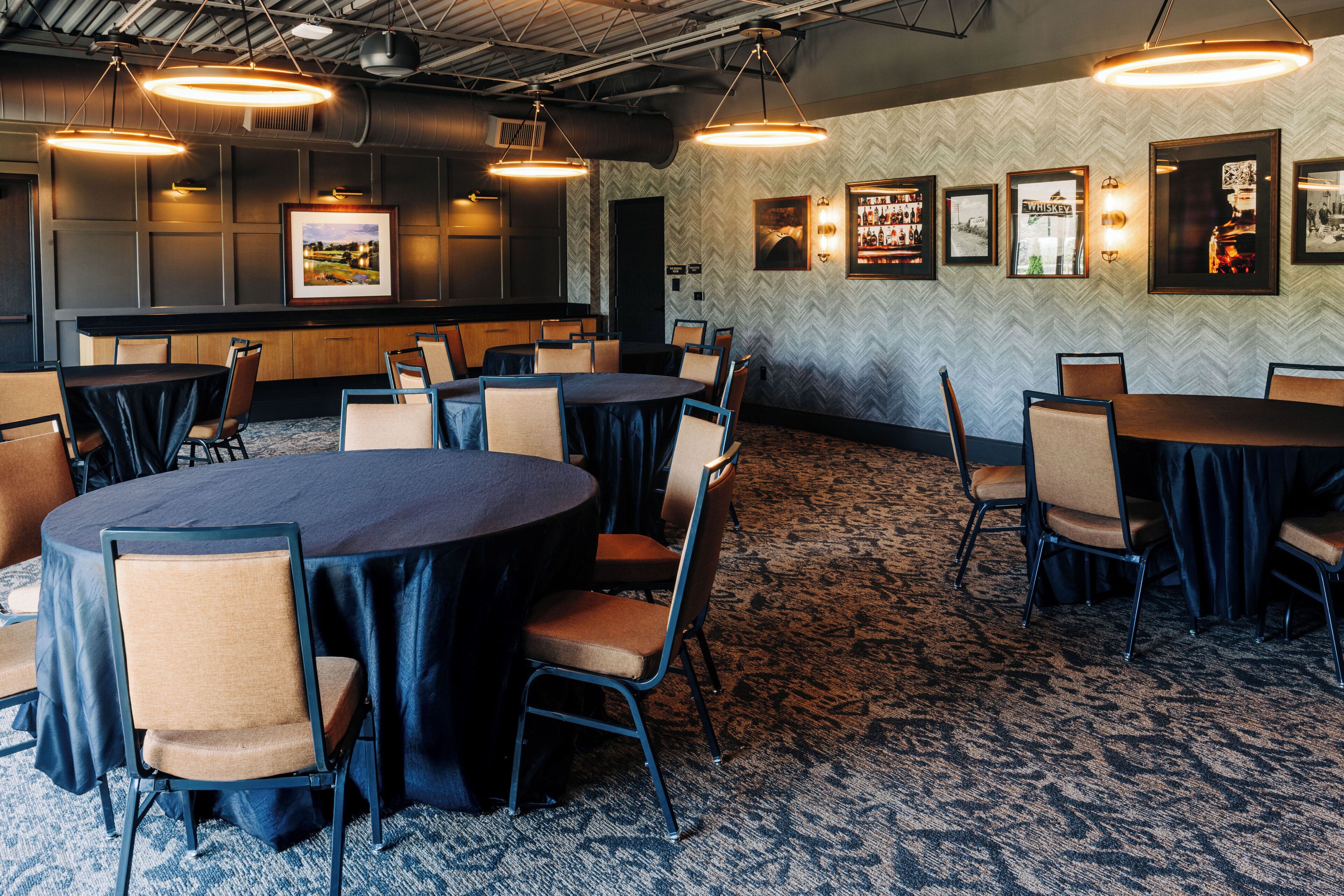 A conference room with round tables and chairs, a patterned carpet, and framed pictures on the walls.