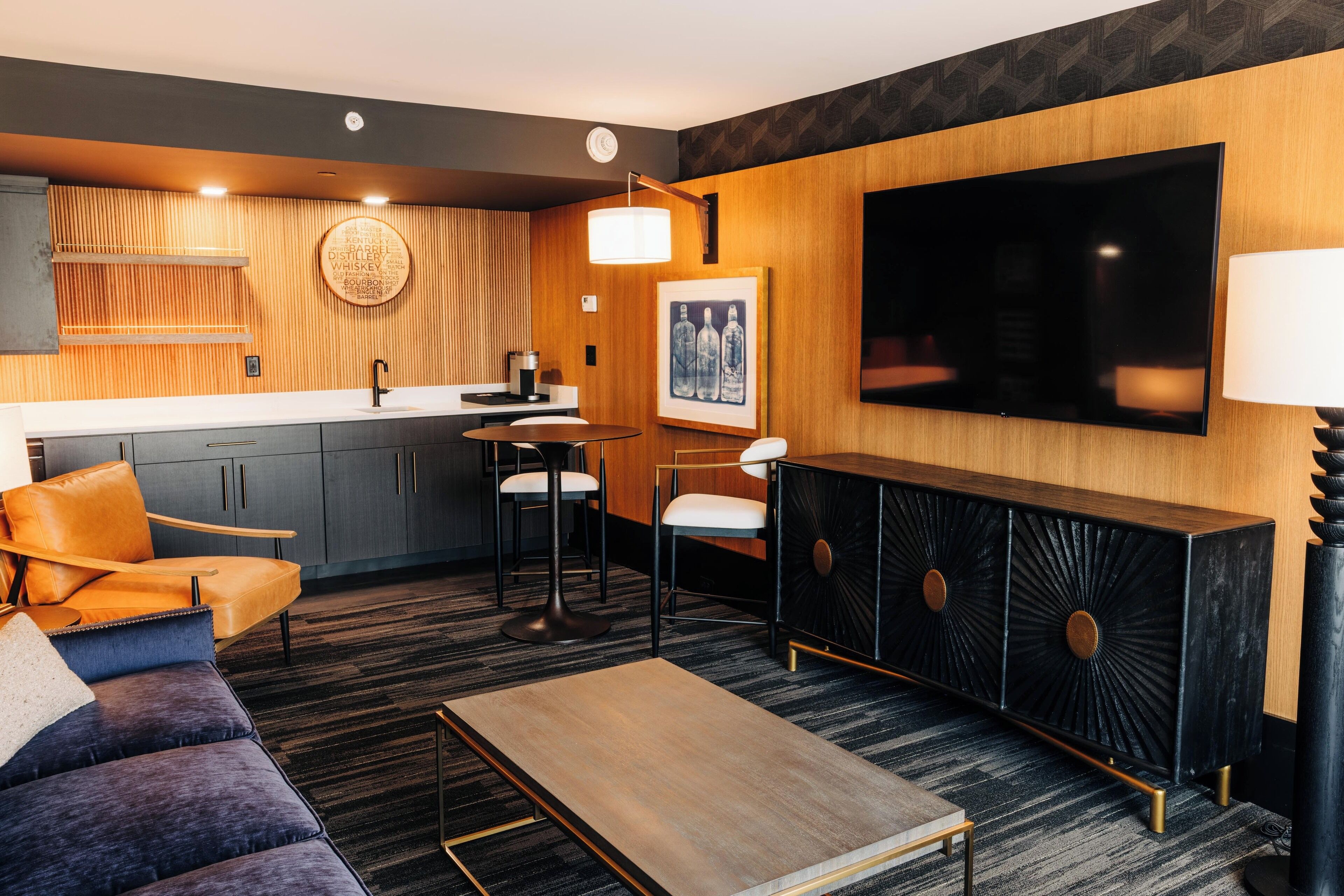 Une chambre d’hôtel moderne dotée d’un coin cuisine, d’un canapé, d’une table à manger et d’un téléviseur fixé au mur.