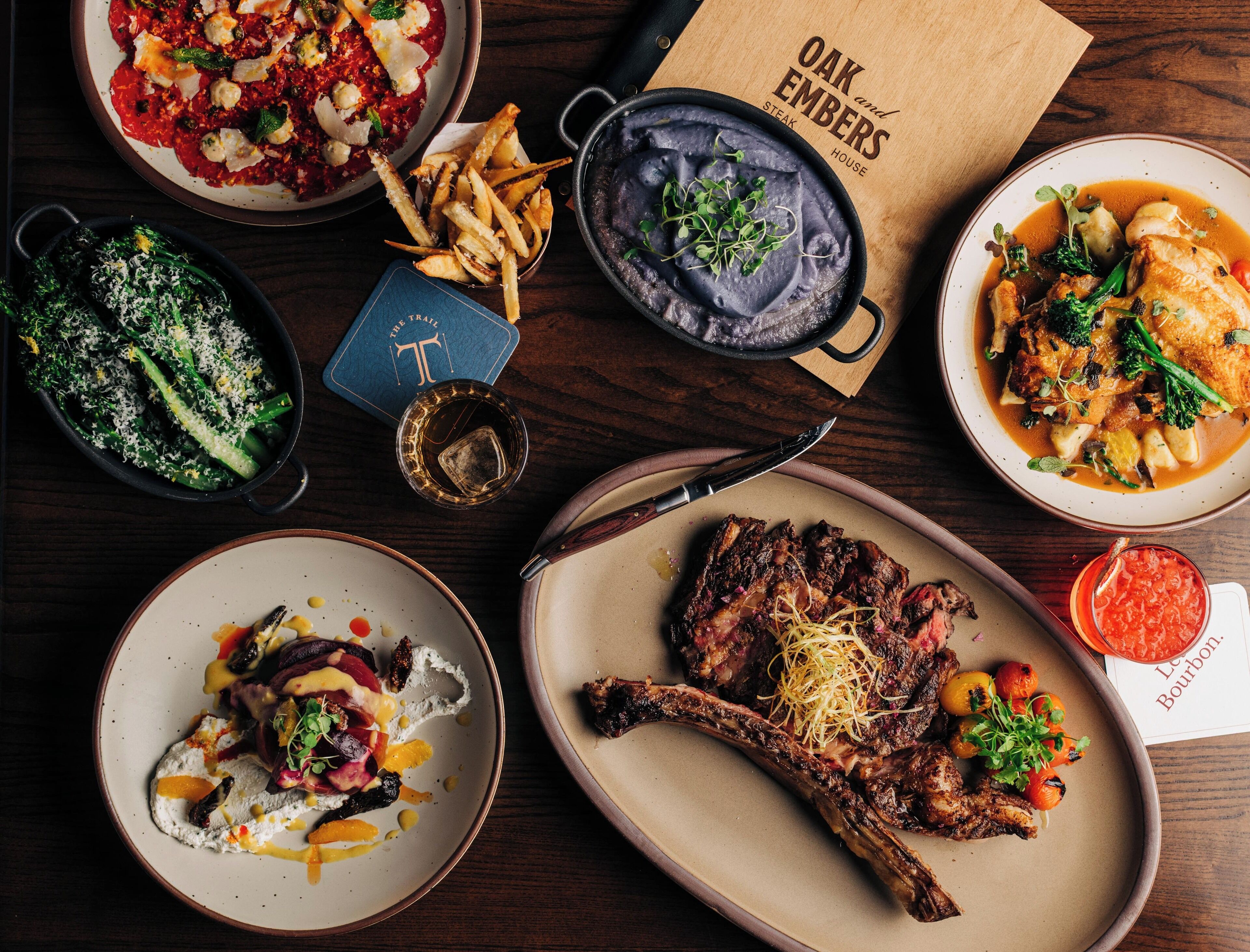 A variety of dishes on a wooden table, including steak, pasta, and vegetables.