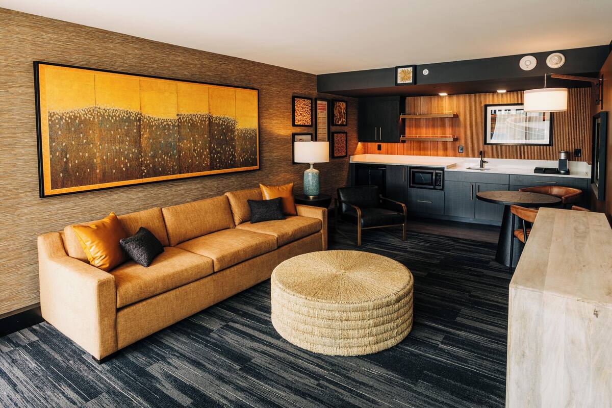 A modern hotel room with a sofa, ottoman, and a dining table.