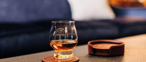 A clear glass of whiskey on a coaster with a leather case beside it on a wooden table.
