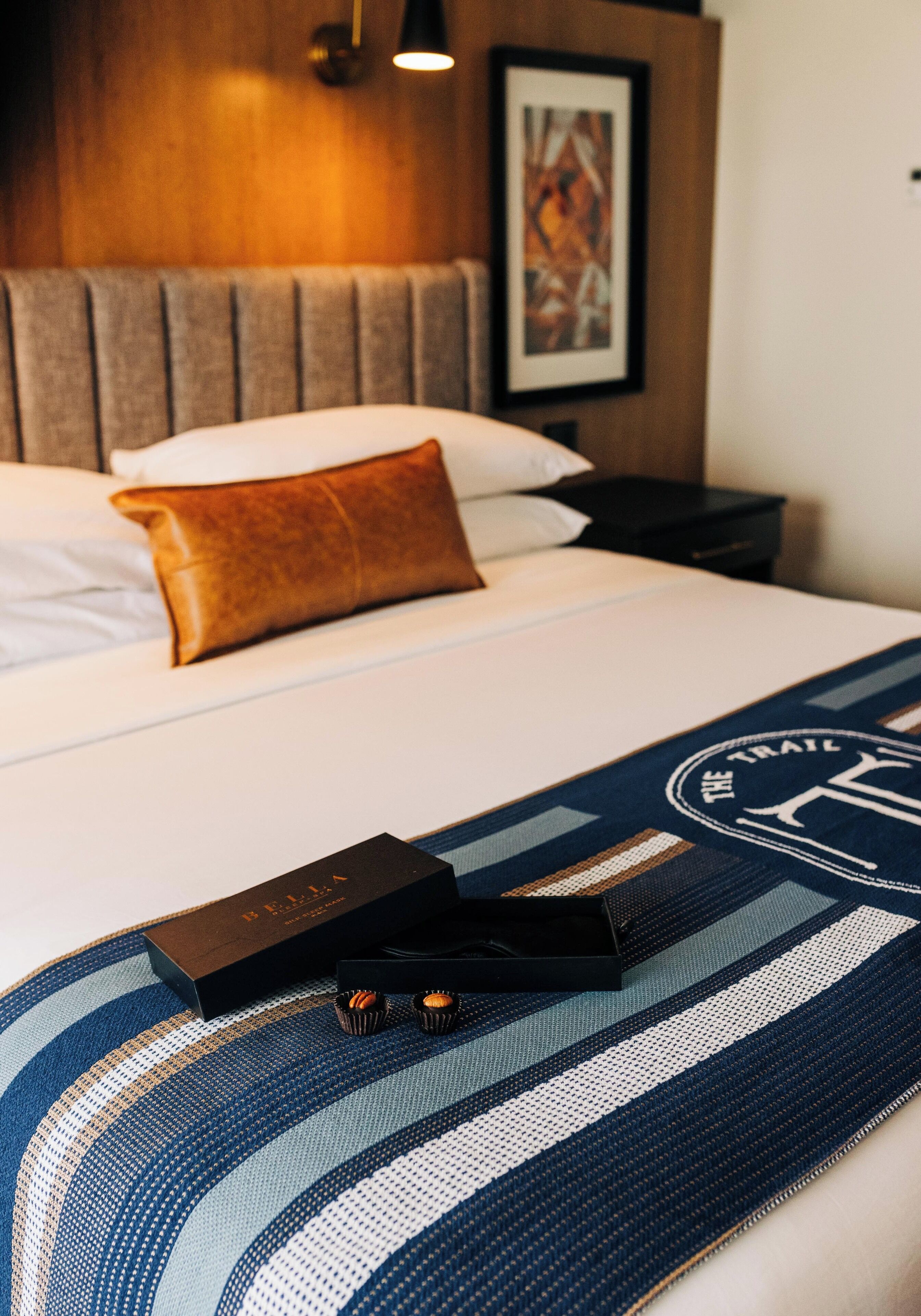 Una cama bien hecha con una colcha a rayas, una almohada marrón y una caja con un logotipo.