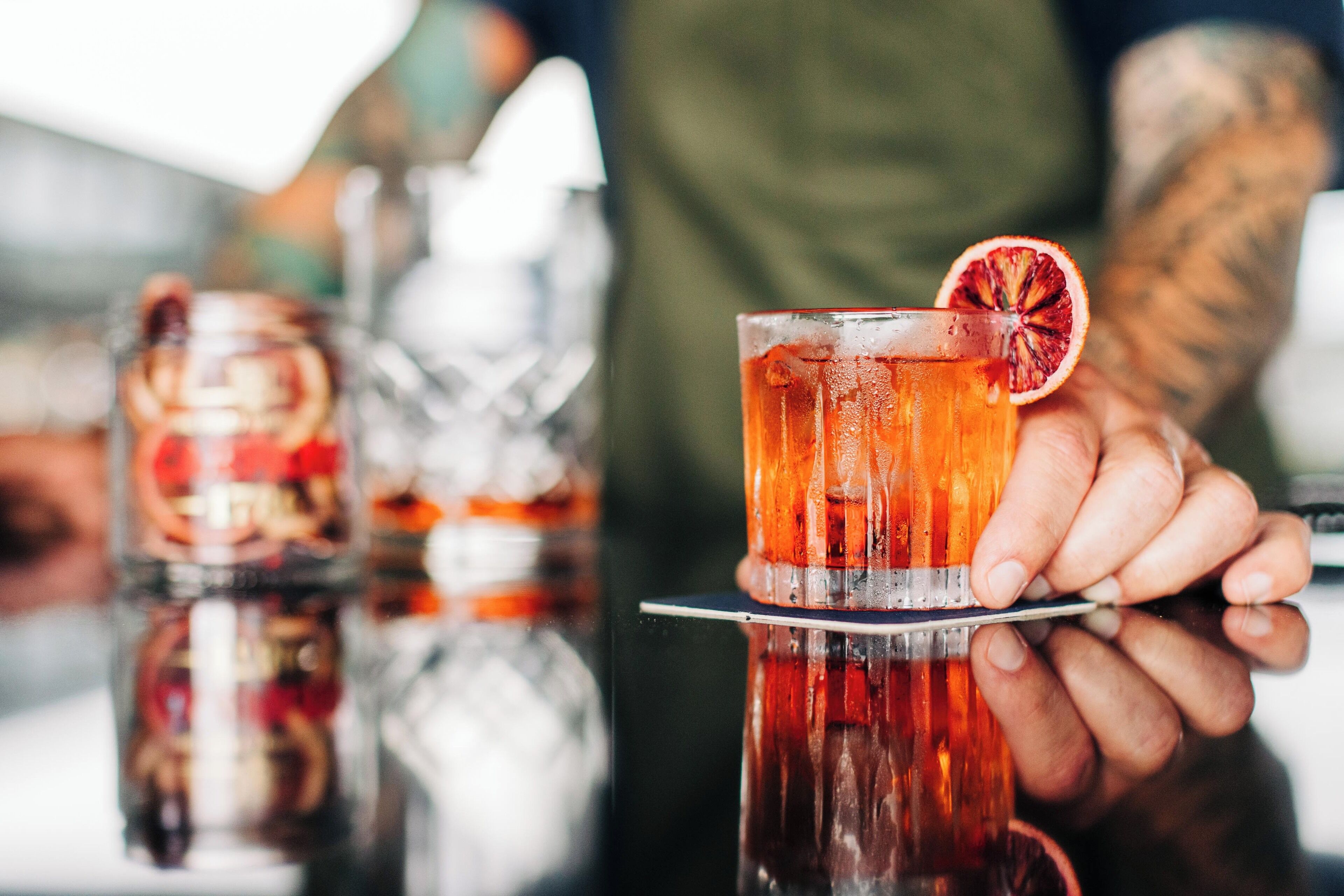 Gros plan d’une main tenant un verre sur le bord duquel est posée une tranche d’orange sanguine.