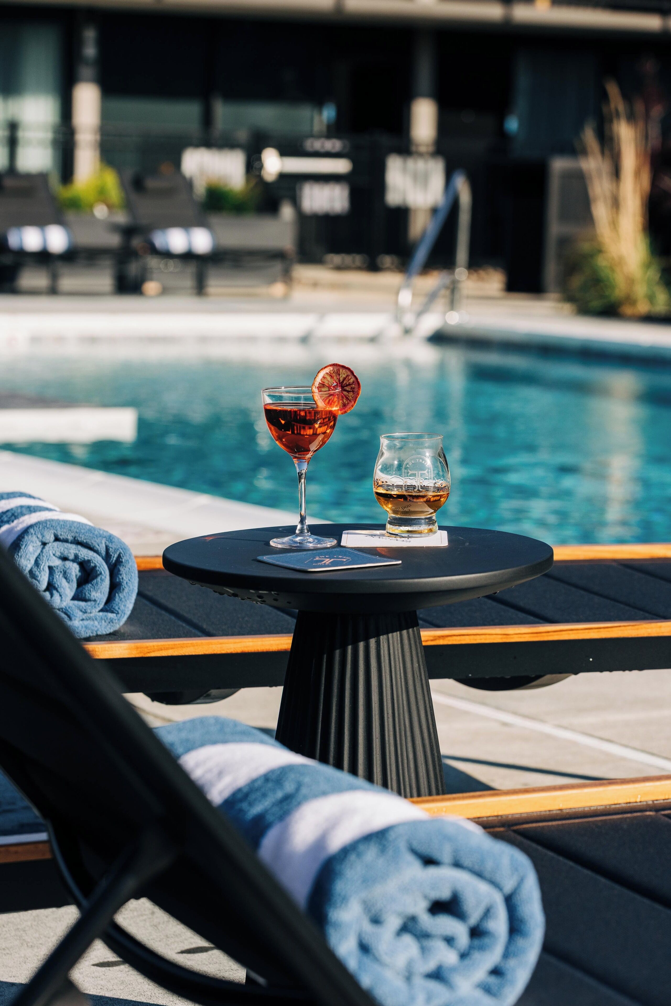Et poolområde med to liggestole, et bord med drikkevarer og en pool i baggrunden.