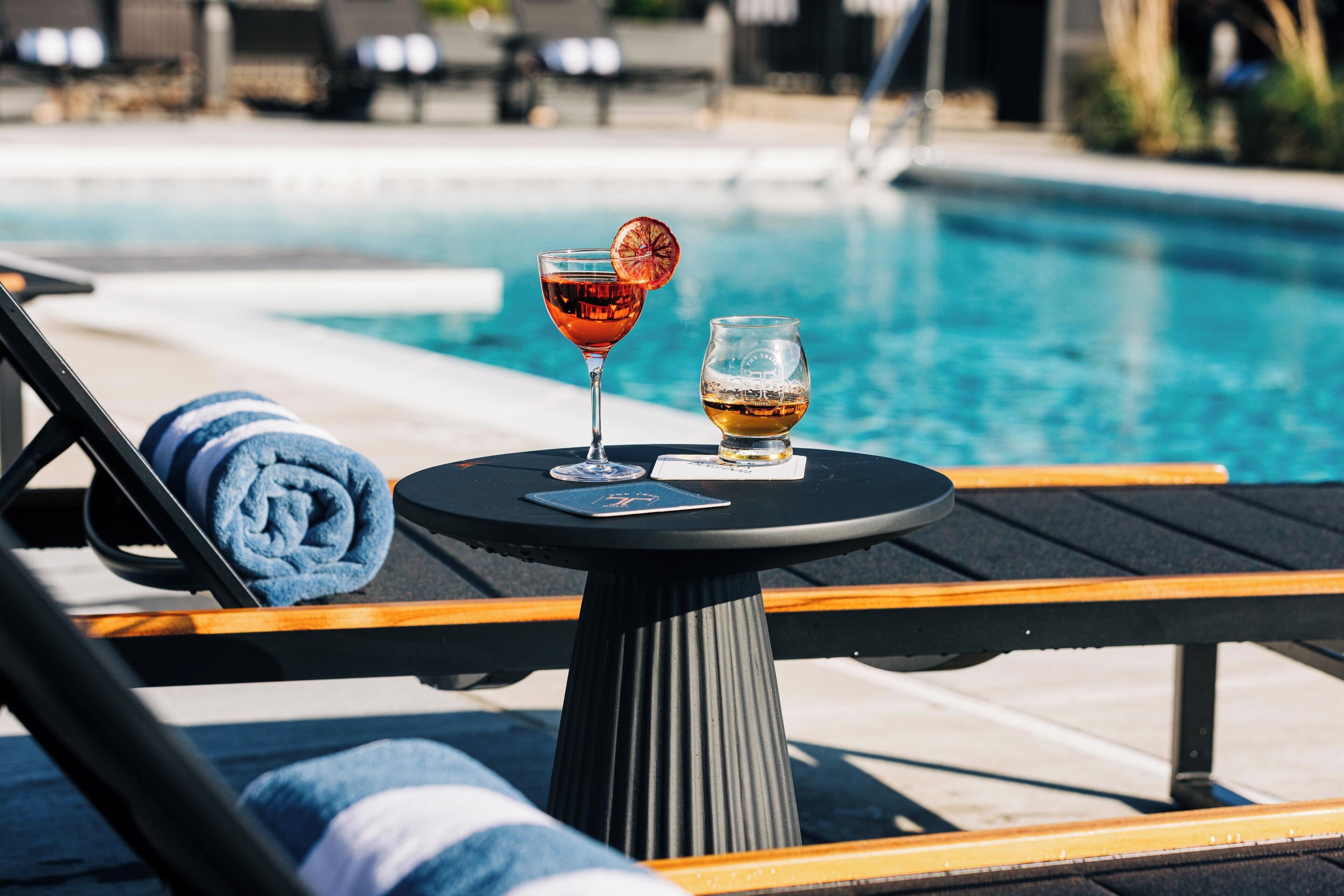 Ein Liegebereich am Pool mit Tisch, zwei Getränken und einem Handtuch.