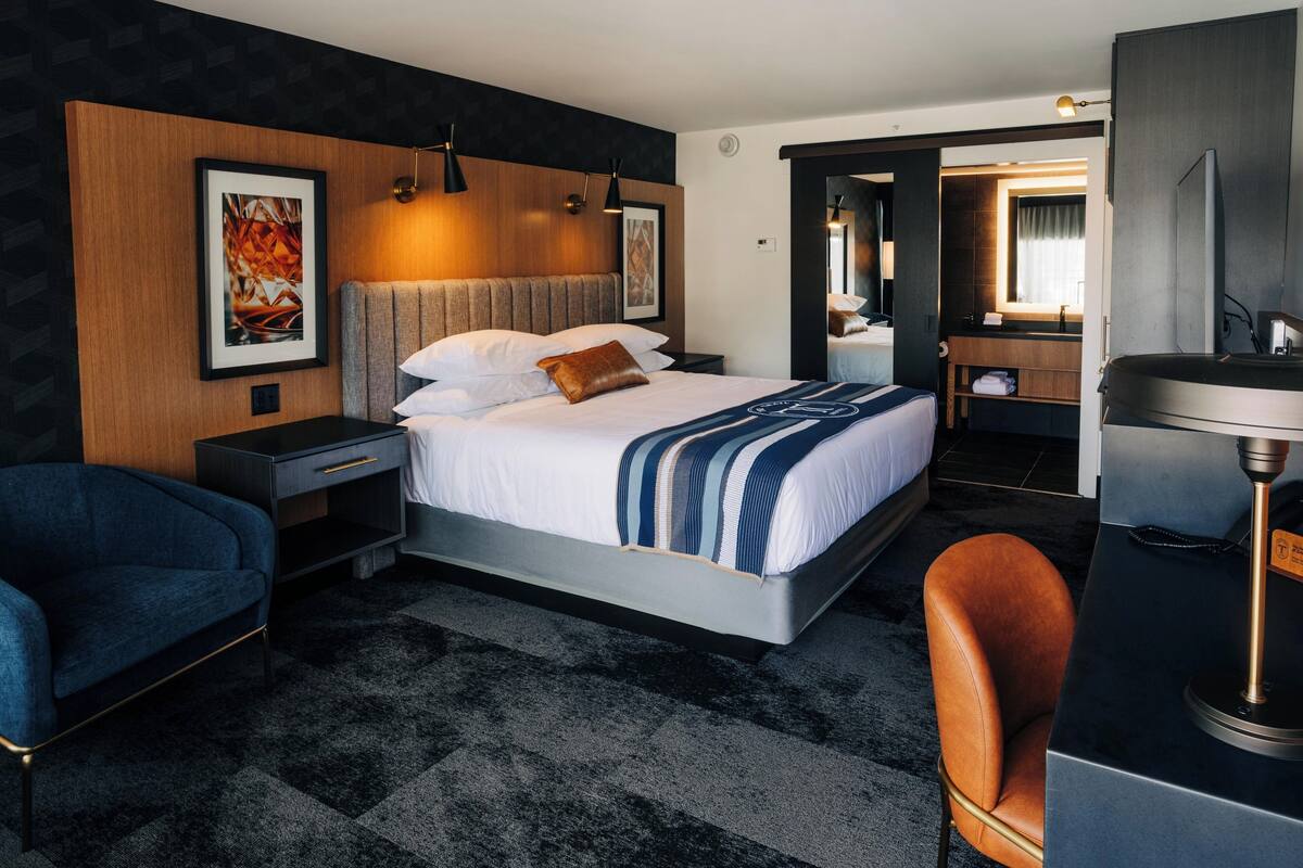 A modern hotel room with a large bed, a desk, a chair, and a bathroom visible through an open door.