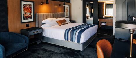 A modern hotel room with a large bed, a desk, a chair, and a bathroom visible through an open door.