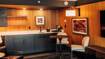 Ein modernes Hotelzimmer mit einer Wandpaneele aus Holz, einer Küchenzeile, einem runden Tisch und einer Bar.