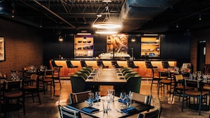 A restaurant with a long communal table and individual booths, a bar area in the background, and a brick wall. - The Trail Hotel (Bardstown)