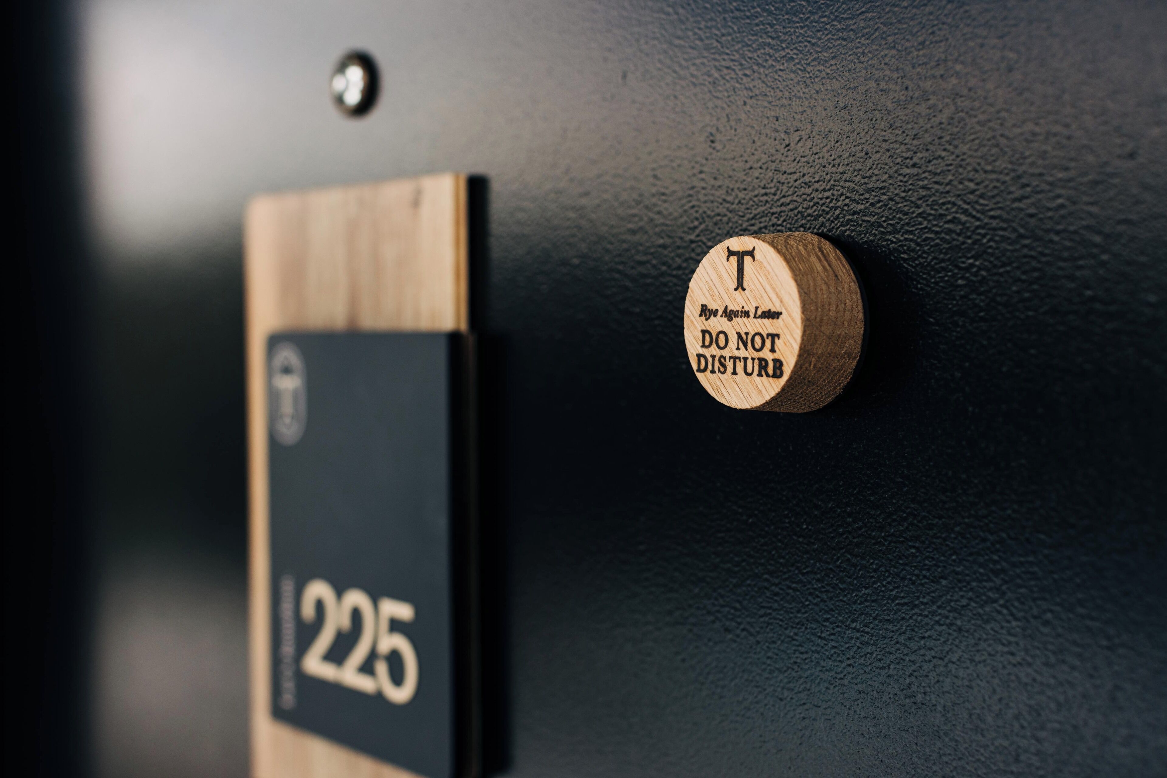 A door with a sign that reads "225" and a round wooden plaque with the text "T DO NOT DISTURB."
