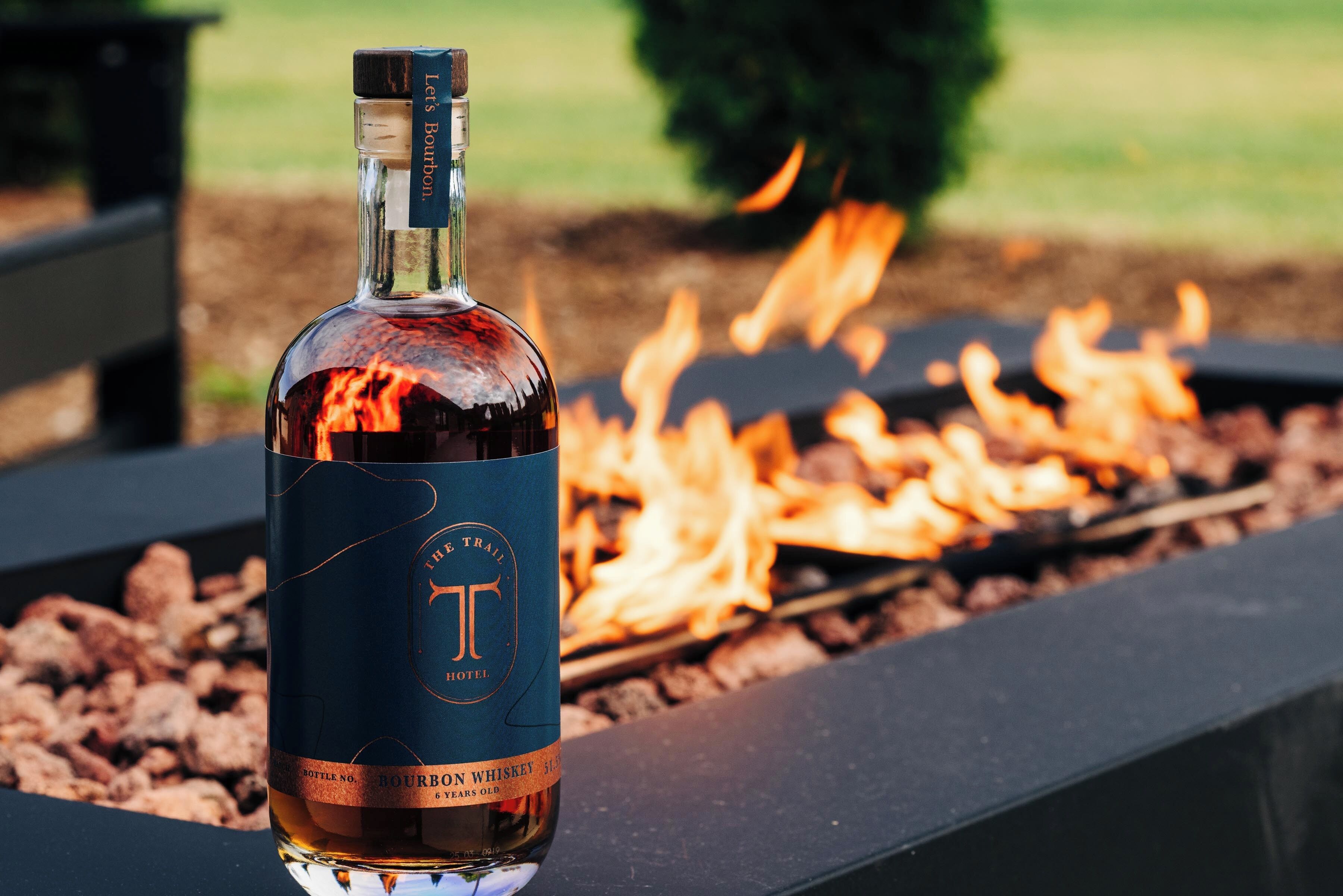A bottle of bourbon whiskey on a grill with flames in the background.