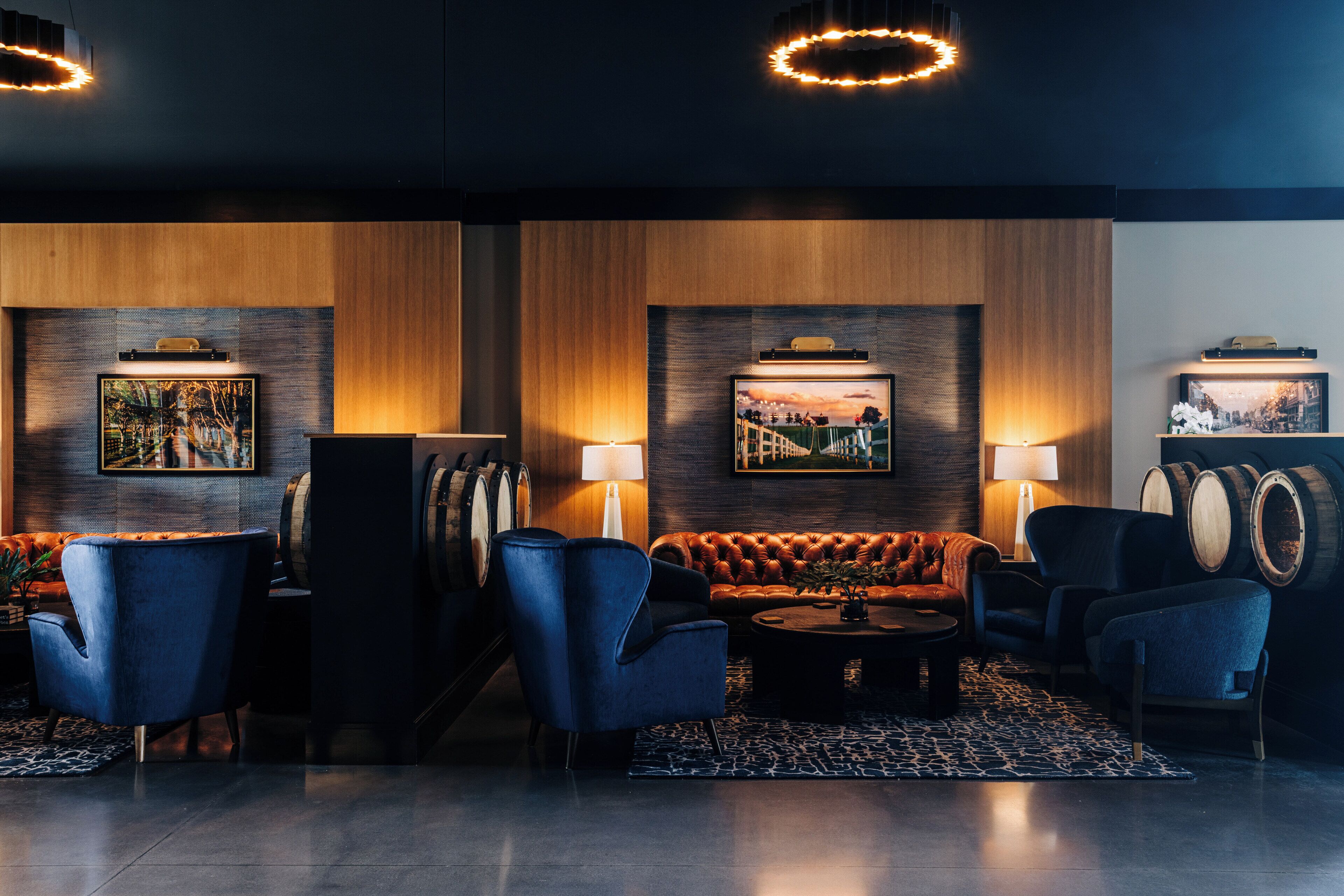 A modern lounge area with a leather sofa, blue armchairs, and a coffee table. There are wooden panel walls and framed pictures on the walls.