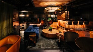 A modern lounge area with leather sofas, a round wooden coffee table, and a bar with stools. - The Trail Hotel (Bardstown)