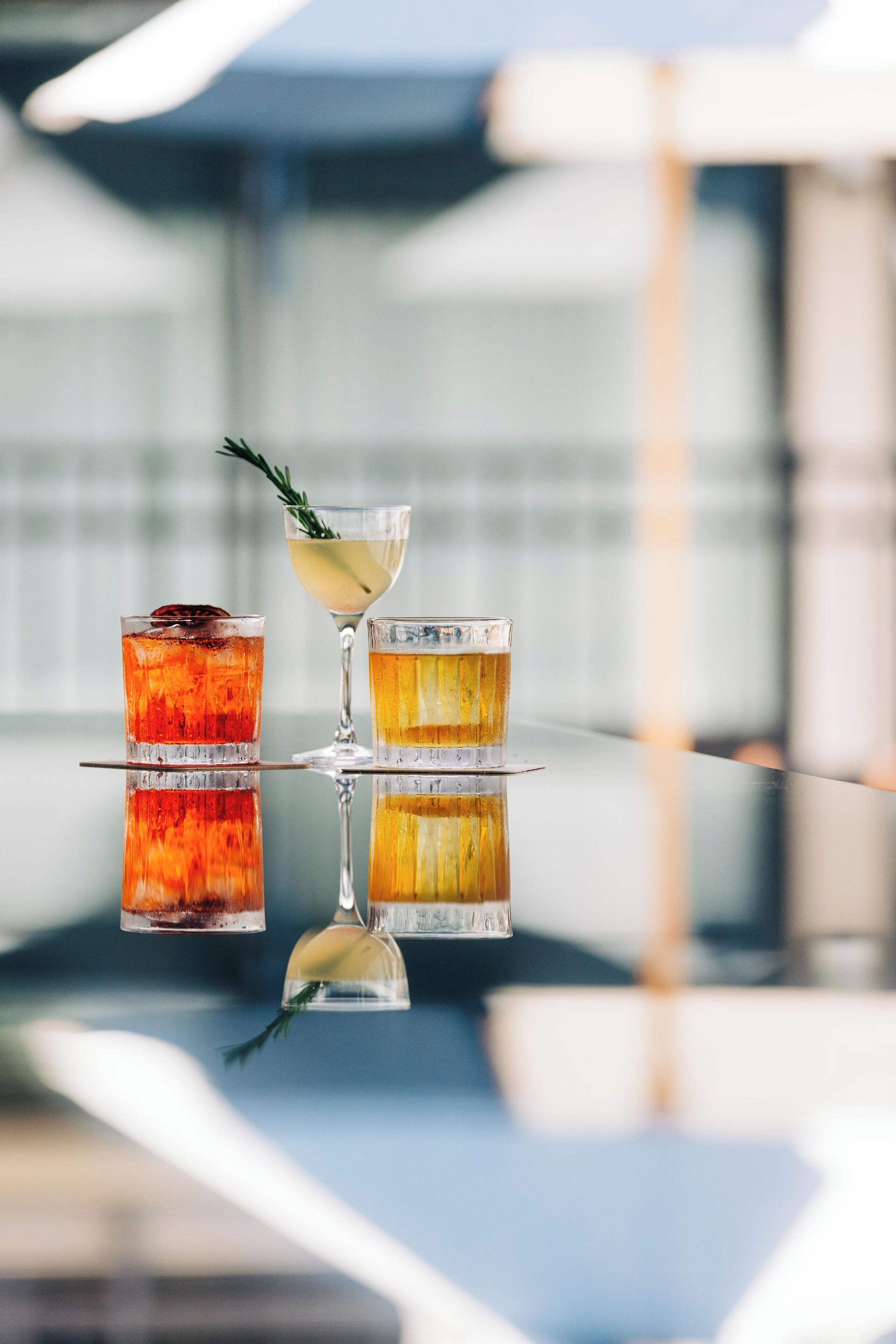 Three cocktails on a reflective surface with a blurred background.