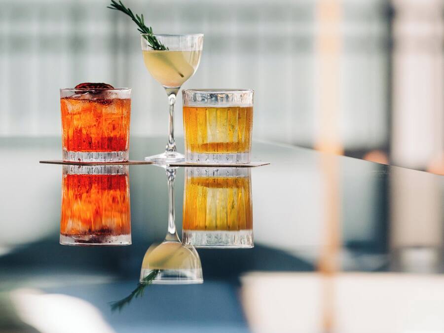 Three cocktails on a reflective surface with a blurred background.