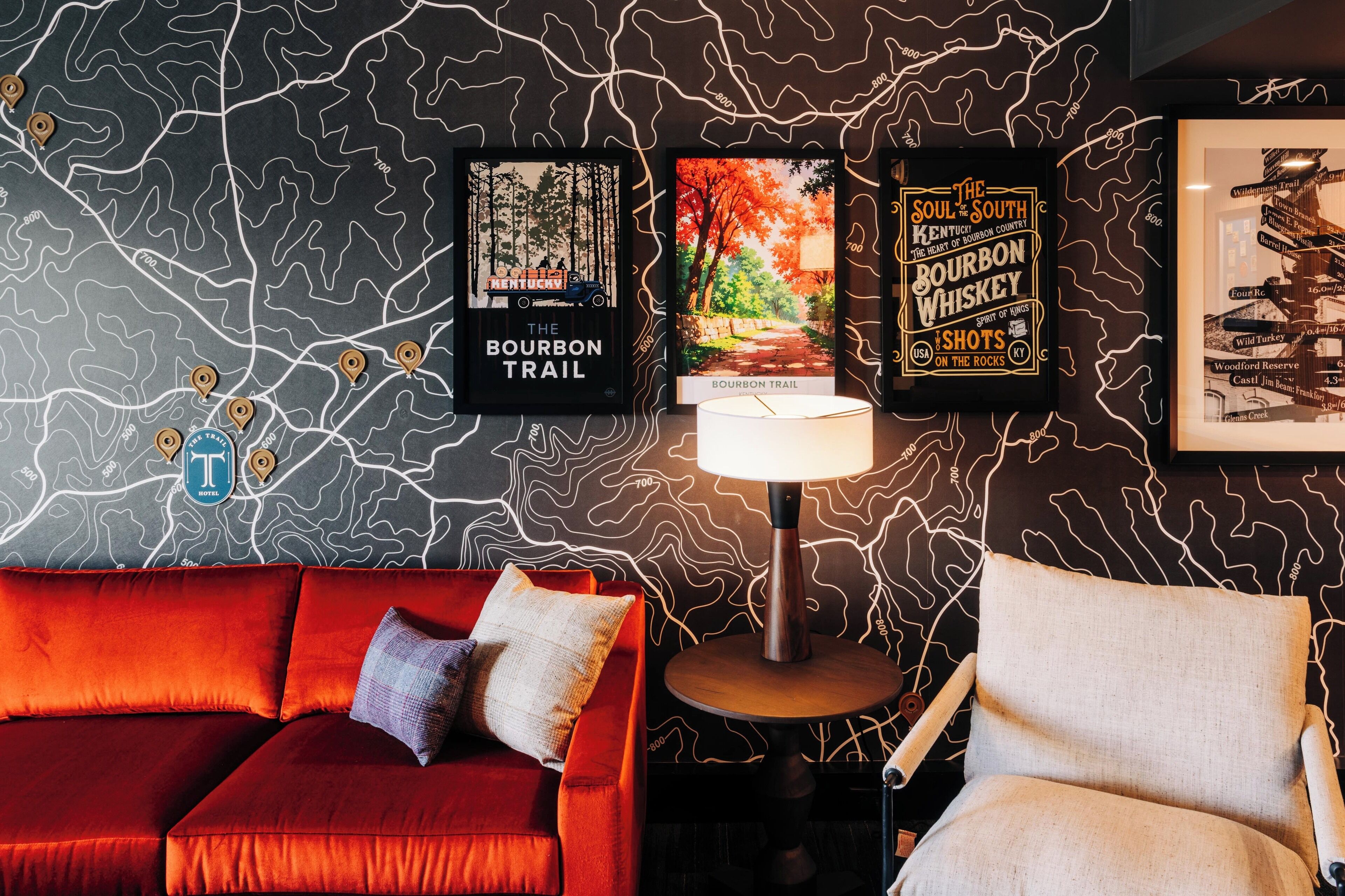 A room with a red sofa, a round table with a lamp, and two framed posters on the wall.