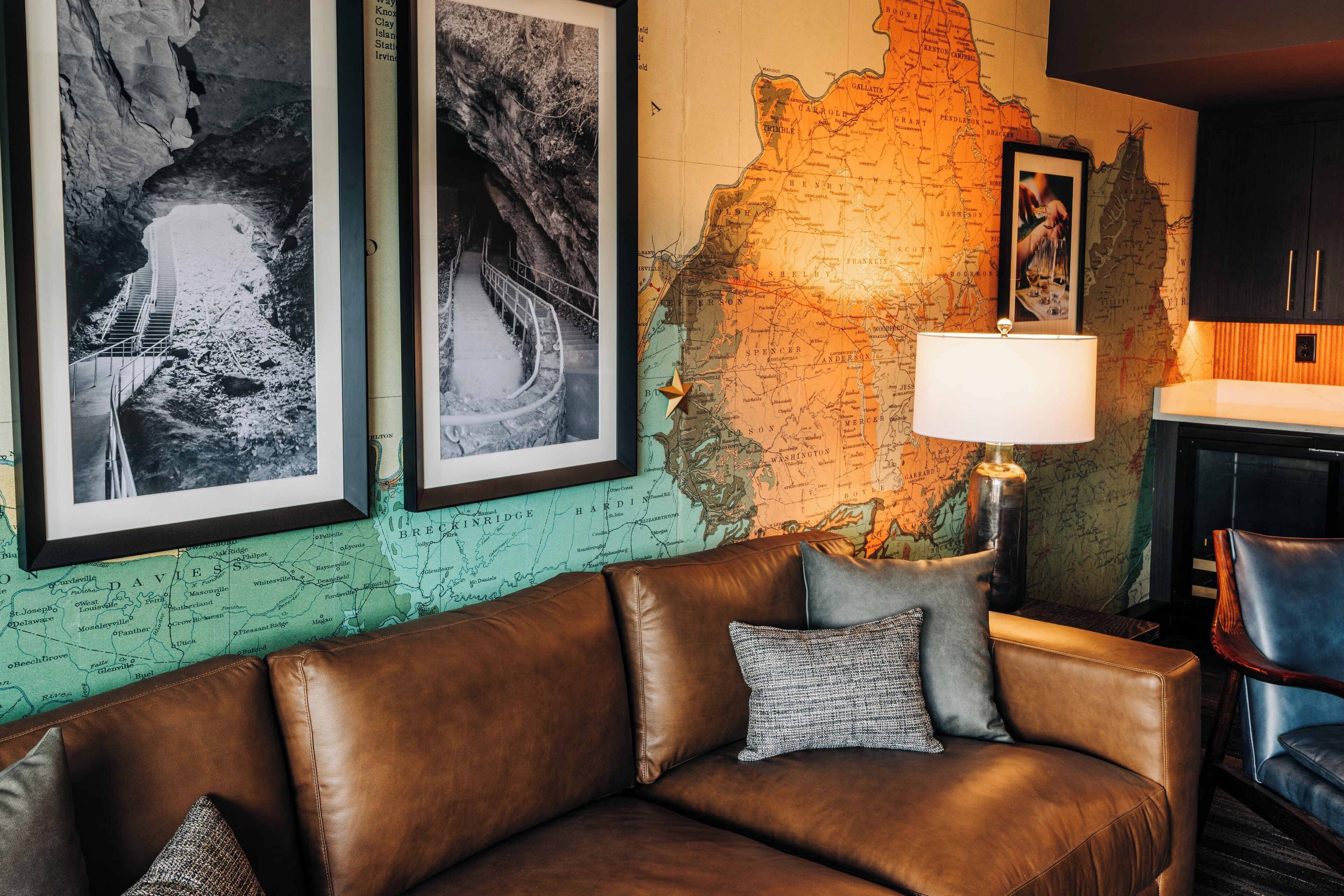 Una habitación con un sofá de cuero marrón, un mapa en la pared y fotografías blanco y negro enmarcadas.
