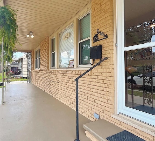 A building with a brick facade, a covered porch, and a large window with a view of the street.