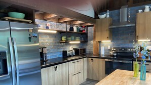 Una cocina moderna con refrigerador de acero inoxidable, armarios de madera, encimera negra y una mesa de comedor de madera con jarrones.