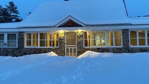 Un edificio cubierto de nieve con fachada de piedra, ventanas grandes y una entrada iluminada.