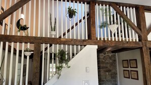 Una escalera de madera con barandillas blancas, plantas en macetas y un muro de piedra.