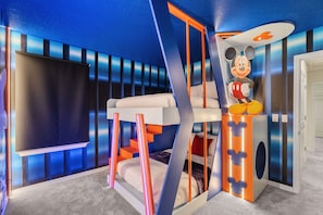 A room with a large flat-screen TV, a bed with Mickey Mouse decor, and a staircase with orange accents. - Ultimate 10 Bed Luxury Retreat With Epic Playroom (Clermont)