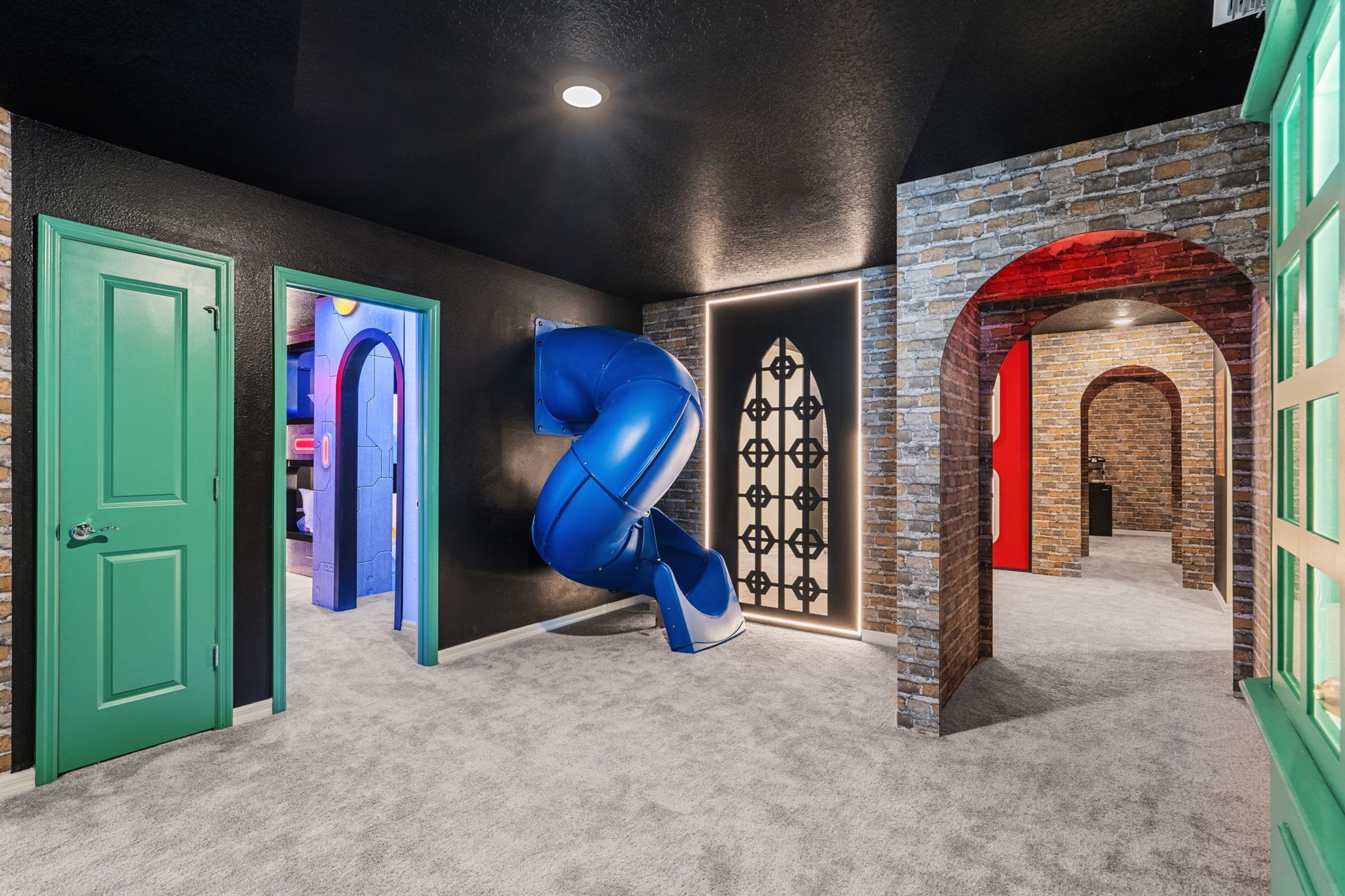 Un couloir avec une porte verte, une structure bleue aux lignes courbes et un mur de briques surmonté d’une arche rouge.