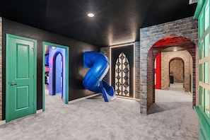 A hallway with a curved blue structure, green doors, and brick walls. - Ultimate 10 Bed Luxury Retreat With Epic Playroom (Clermont)